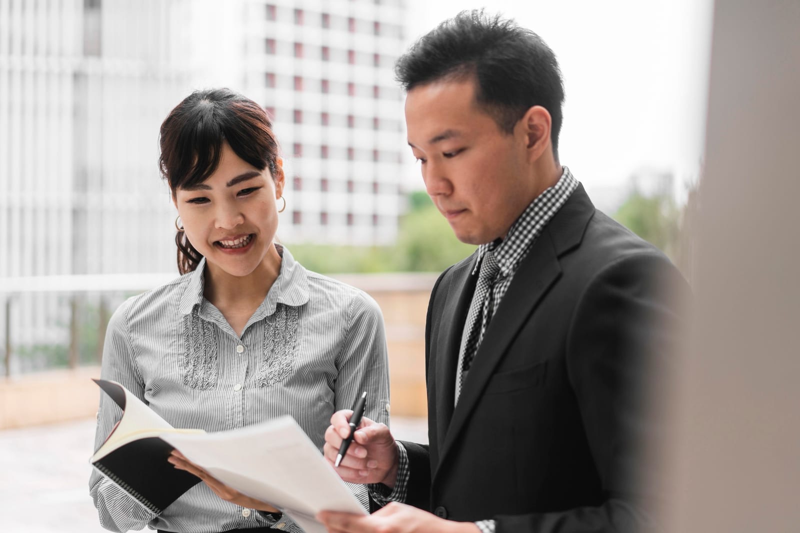 レンガ壁の会議室でホワイトボードの前に立ち資料を示す女性と、着席して聞く二人